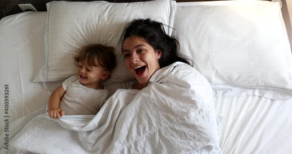 Toddler and mom playing hide and seek under blanket in bed. Peepaboo play. Mother and baby cuddling in bed together Toddler and mom playing hide and seek under blanket in bed. Peepaboo play. Mother and baby cuddling in bed together