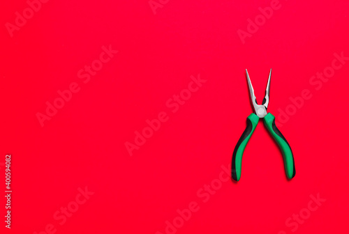 Quality green building pliers tool to compress something or repair a car or house on red background. Do it yourself instrument. Banner for advertising construction shop with copy space. Business card