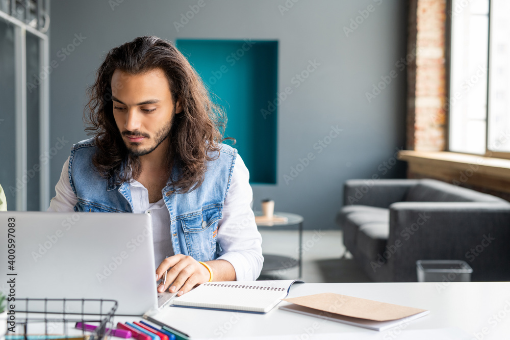 Mixed-race businessman or office manager sitting by workplace in front of laptop Mixed-race businessman or office manager sitting by workplace in front of laptop