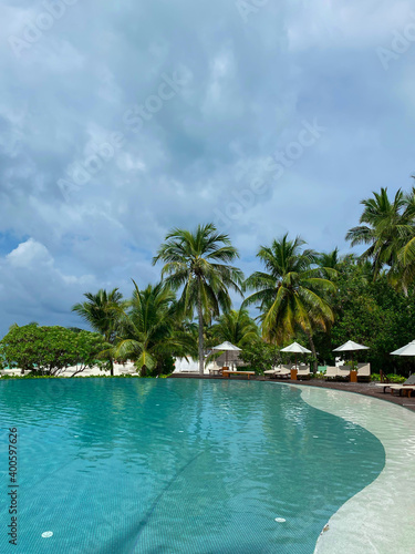 Outdoor tourism landscape. Luxurious beach resort with swimming pool, palm trees and blue sky. Summer travel and vacation background concept. Maldives. Vertical image.