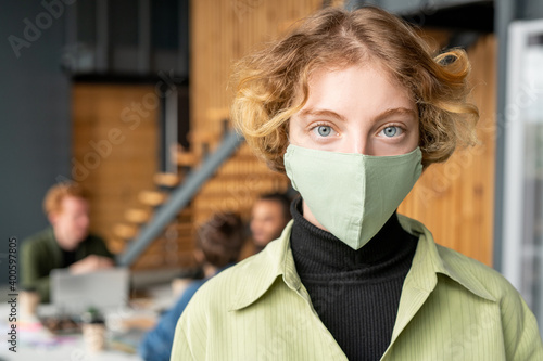 Young blond female office worker in casualwear and protective mask