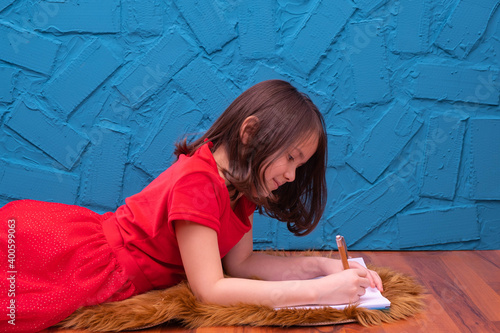 a little girl in a red dress lies on the floor and draws something