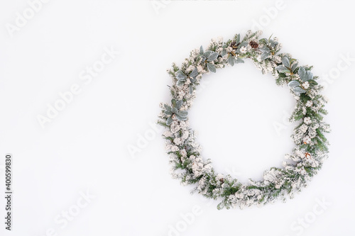Christmas wreath made of natural fir branches hanging on white wall. Garland with natural ornaments: cones, cotton flowers, mistletoe. New year and winter holidays. Christmas decor. Copy space. Mockup