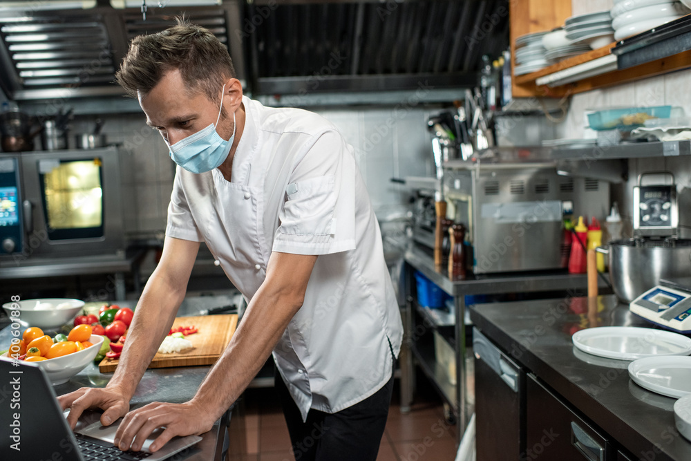 Contemporary chef in uniform and protective mask surfing for online recipes Contemporary chef in uniform and protective mask surfing for online recipes