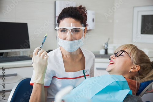 Female dentist in protection mask holding syringe with anesthetic. Stomatologist and patient at clinic office. Toothcare concept
