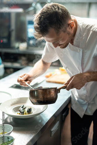 Chef in uniform bending by kitchen table and putting boiled mussels on plate