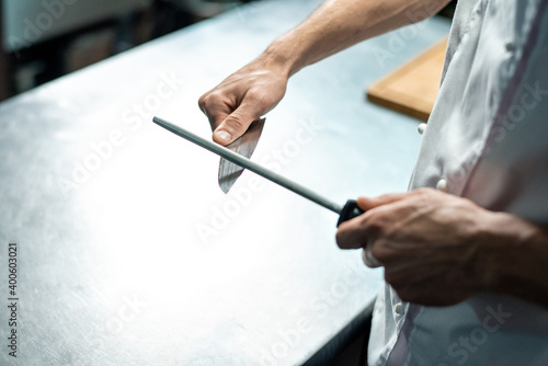 Hands of young male chef of modern restaurant in white uniform sharpening knife © pressmaster