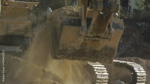 Excavator bucket scoops the ground filling a truck body. Close-up. Construction site working.