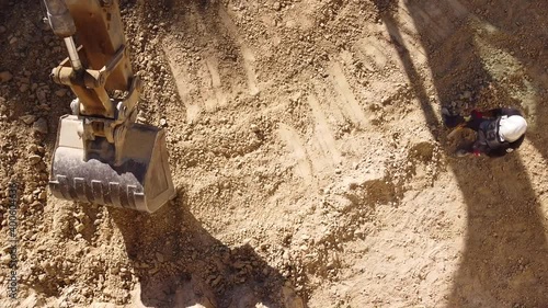 Earth mover's scoop excavates the ground. Unrecognized worker controlling the process. View from above of construction site working.