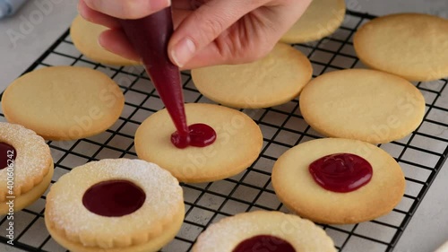 Female hands put jam on cookies from a pastry bag. Female hands a making homemade biscuit shortbread cookies with jam. Kurabye cookies with raspberry jam. Christmas cookies with jam.
