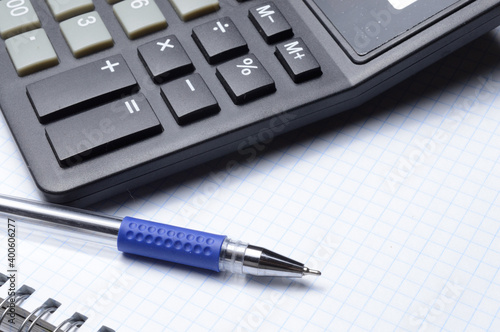 a ballpoint pen and a micro calculator lie on a squared notebook. close-up.