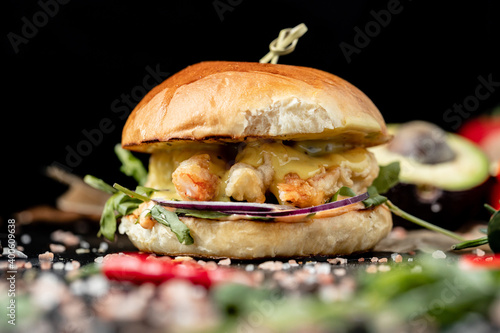 Large chicken, beef and shrimp burgers Beef burger with cheese, tomatoes, red onions, cucumber and lettuce on black slate over dark background. Unhealthy food