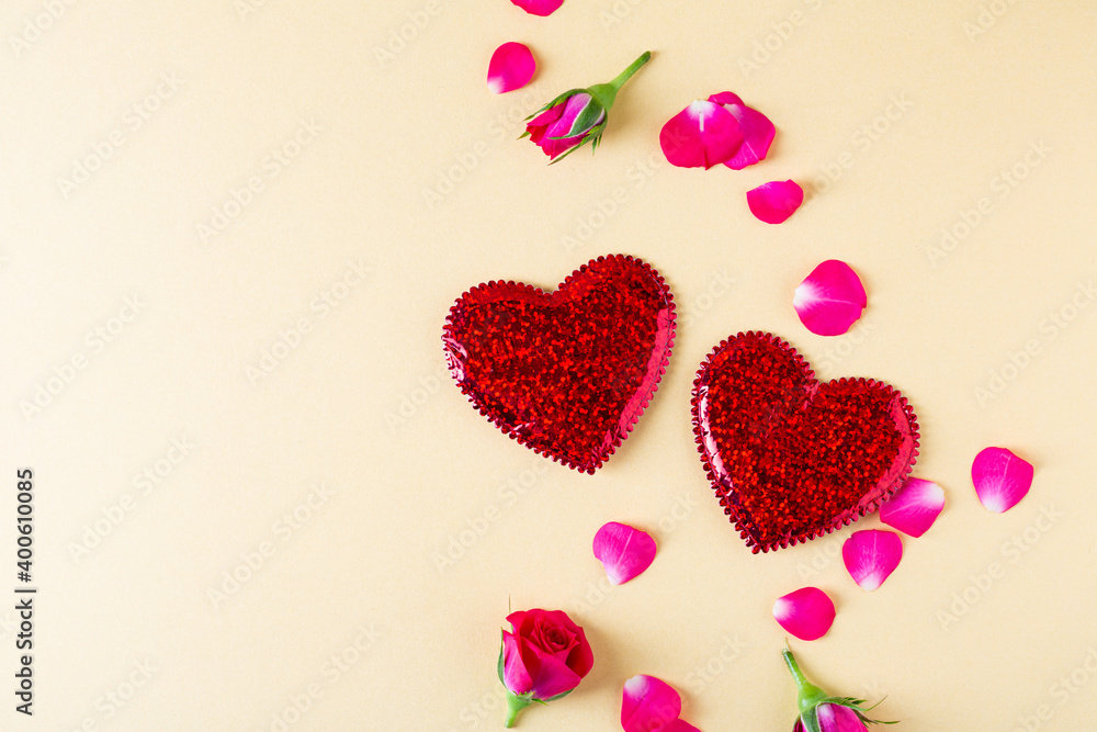 Composition with two red hearts and roses petal on golden background