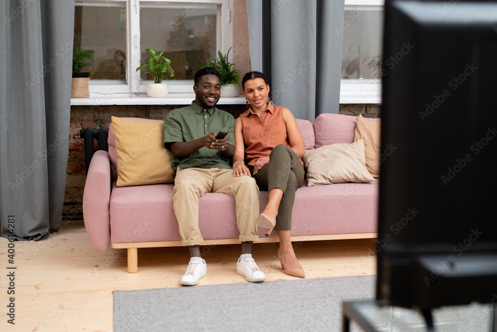 Happy African teenage boy with remote control and girl sitting on couch