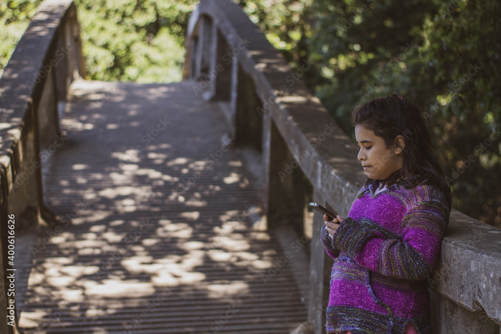 Selective focus Latin child with cell phone on a bridge Selective focus Latin child with cell phone on a bridge