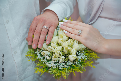 The newlyweds put their hands on a engagement white bouquet of white roses . the bride put her hand on her husband's hand with wedding rings