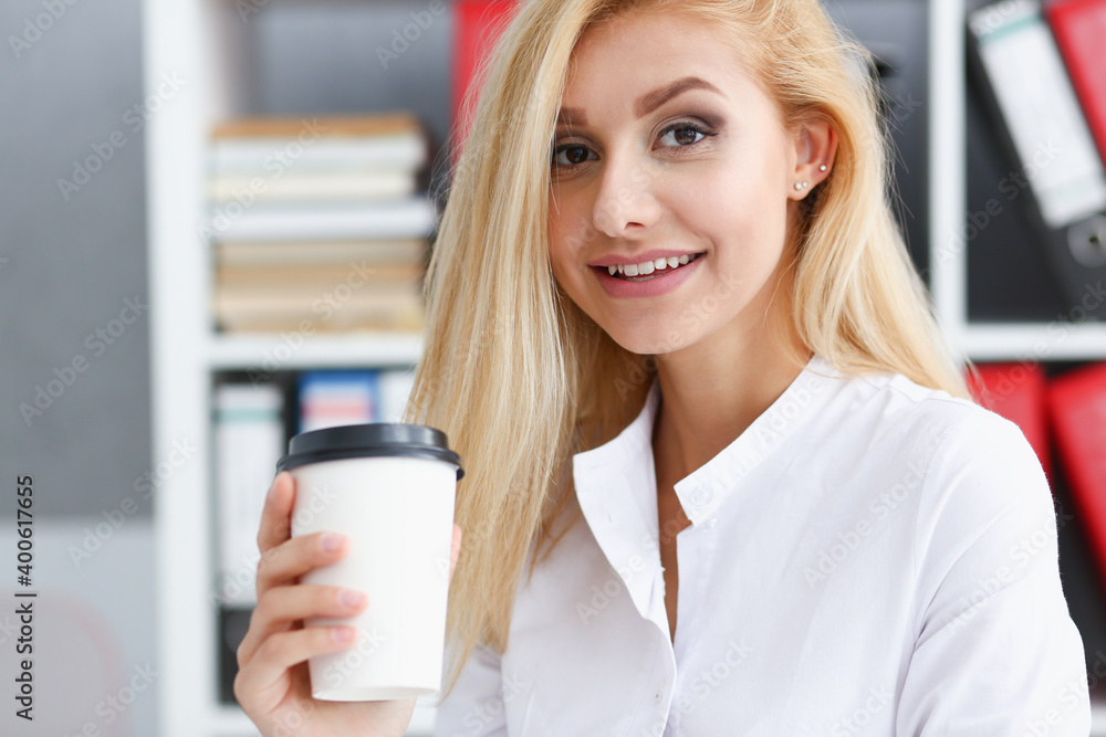 Smiling business woman drinking coffee from a paper cup in the office portrait looking into the camera holding in her hand and resting during a break Smiling business woman drinking coffee from a paper cup in the office portrait looking into the camera holding in her hand and resting during a break