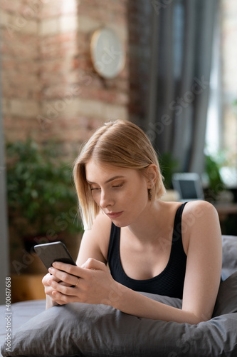 Young restful female with smartphone texting or scrolling through online news