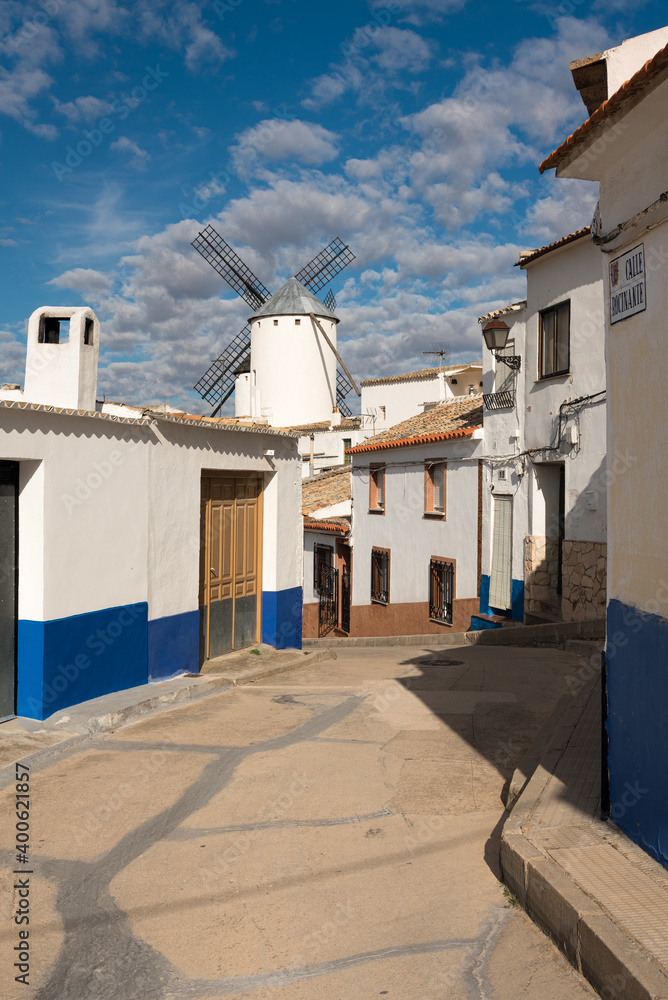 Cobbled street, white houses and windmills in the old town of Campo de Criptana on a day with blue sky and clouds, Ciudad Real, Spain