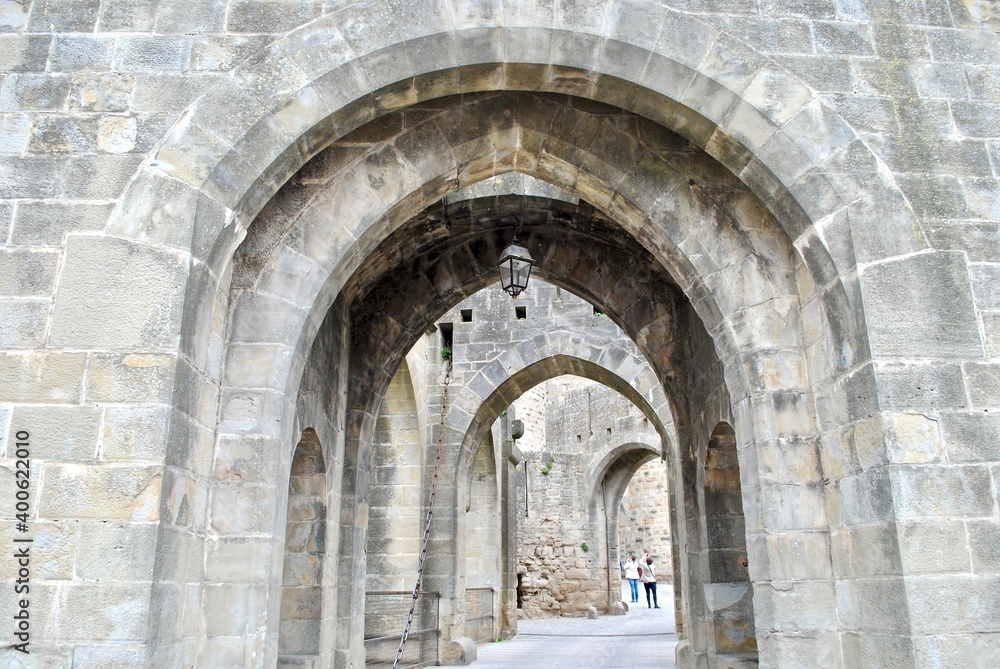 A series of arched, stone passageways in Carcassonne, a French fortified city in the region of Occitanie. The citadel, known as the Cité de Carcassonne, is a medieval fortress and UNESCO site.