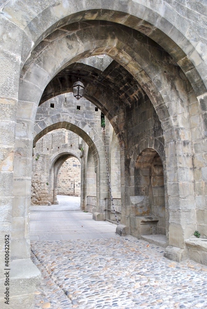 A series of arched, stone passageways in Carcassonne, a French fortified city in the region of Occitanie. The citadel, known as the Cité de Carcassonne, is a medieval fortress and UNESCO site.