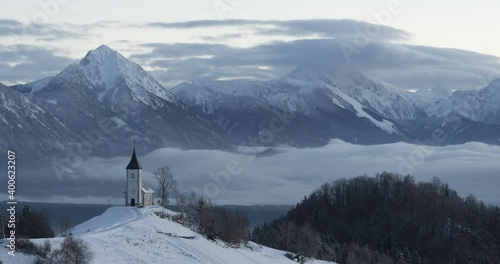 Time lapse of inversion clouds moving in basin, Slovenia. Alps mountains covered with snow in the distance. Famous Jamnik church at colorful sunrise. Wide angle, static shot