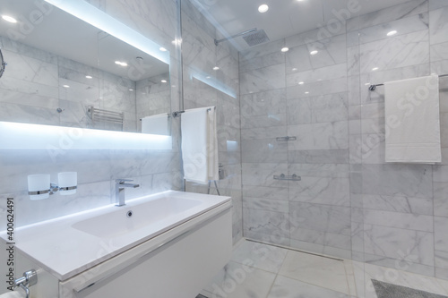 Beautiful modern bathroom with large backlit illuminated mirror  sink  and glass shower