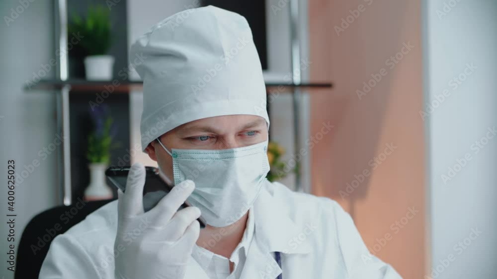 A doctor wearing a medical mask and a medical mask is talking on the phone using a speakerphone. A doctor wearing a medical mask and a medical mask is talking on the phone using a speakerphone.