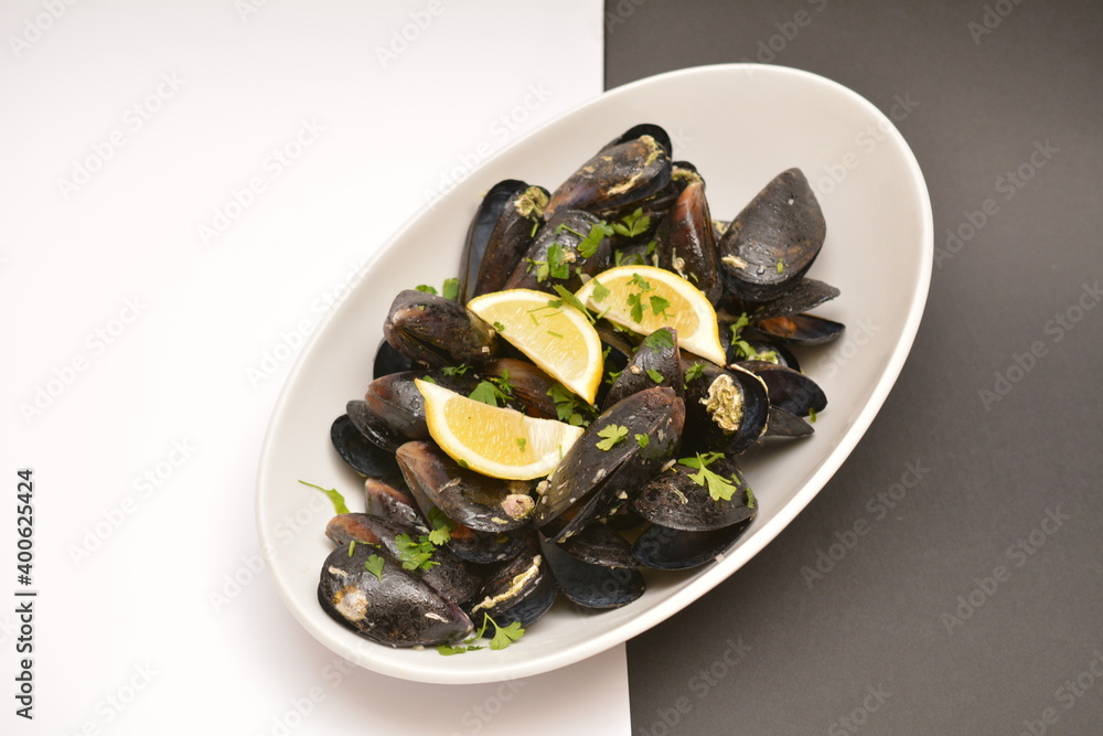 Black mussels on a white oval plate. Decorated with lemon wedges. Located on a black and white background. Can be used in the restaurant menu.