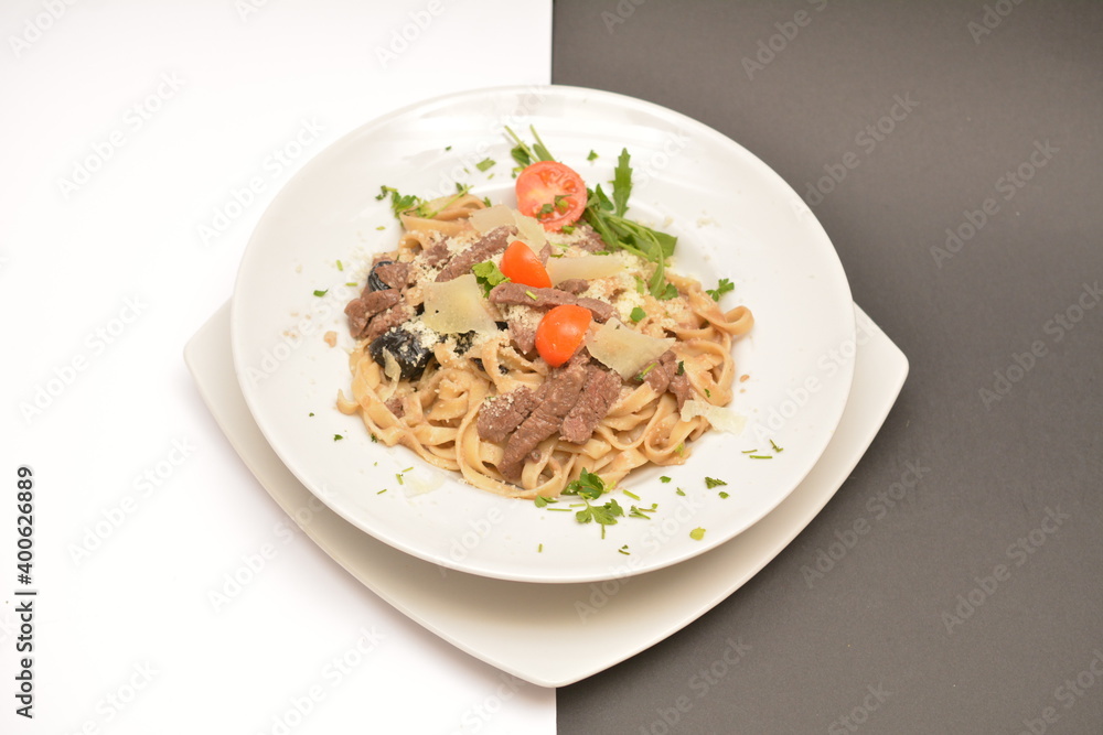 Pasta with beef, prunes and parmesan cheese on a white plate. Located on a black and white background. Can be used in the restaurant menu.