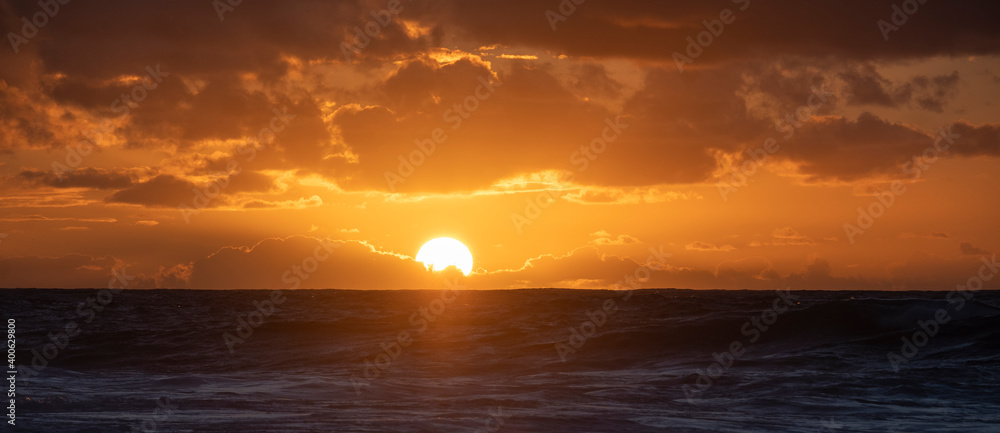 sunset over the sea with big and bright sun and orange colours in the sky