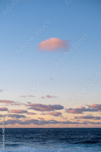sunset over the blue sea with alone pink cloud at the top and others in the blue sky. Vertical shot 