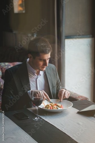 A young attractive man eating cottage cheese pancakes with sour cream and almond flakes and sea buckthorn-orange sauce in an indoor restaurant