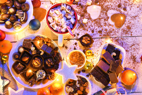 sweet food top view background for merry christmas or new year holiday decoration with night illumination - chocolate candies, tangerines, cookies, marshmallow and cocoa latte on white wood