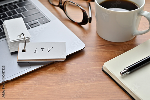 On a desk with a laptop, glasses, coffee, and a notebook, a vocabulary book was placed open There. The word LTV is there. It's an acronym that means Life Time Value. photo