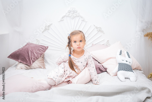 Little girl in a pink dress sits on the bed and hides something behind her back