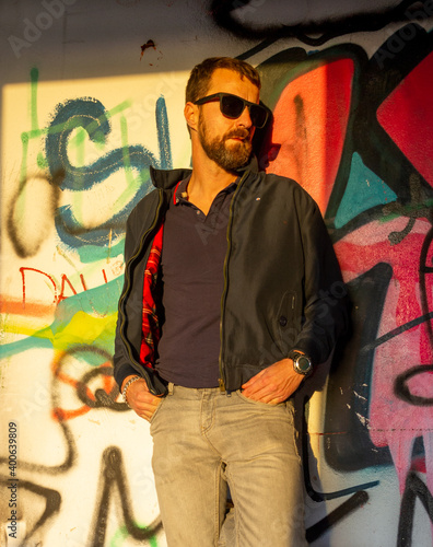 A young man standing by a painted grafitty wall in an abandoned house urbex at the golden hour on a sunny warm day photo