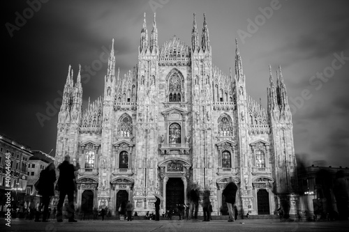 Milan Cathedral - Duomo di Milano - is the gothic cathedral church of Milan, Italy. Shot in the dusk from the square ful of people. Black and white photo.