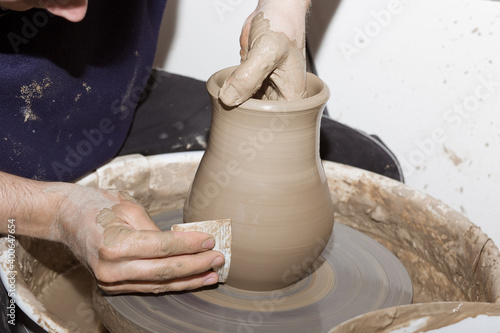 hands of a male potter in apron making a vase from clay