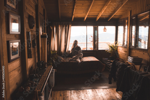 Peaceful young woman reading a book in a comfortable log cabin resting in a beautiful interior room in bed