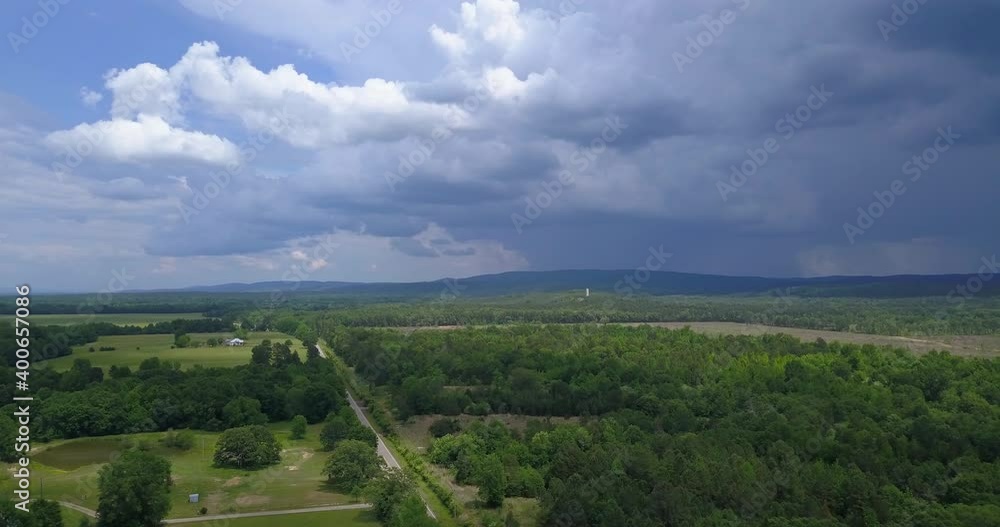 Slow pan left to right aerial shot of a rural summertime landscape and farm land with storm clouds in the distance. Slow pan left to right aerial shot of a rural summertime landscape and farm land with storm clouds in the distance.