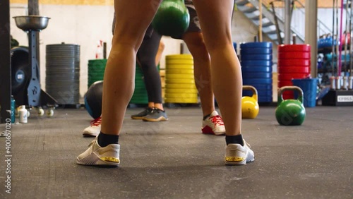 Legs of white people lifting yellow and green kettlebells with colorful weight plates in the background, close shot. photo