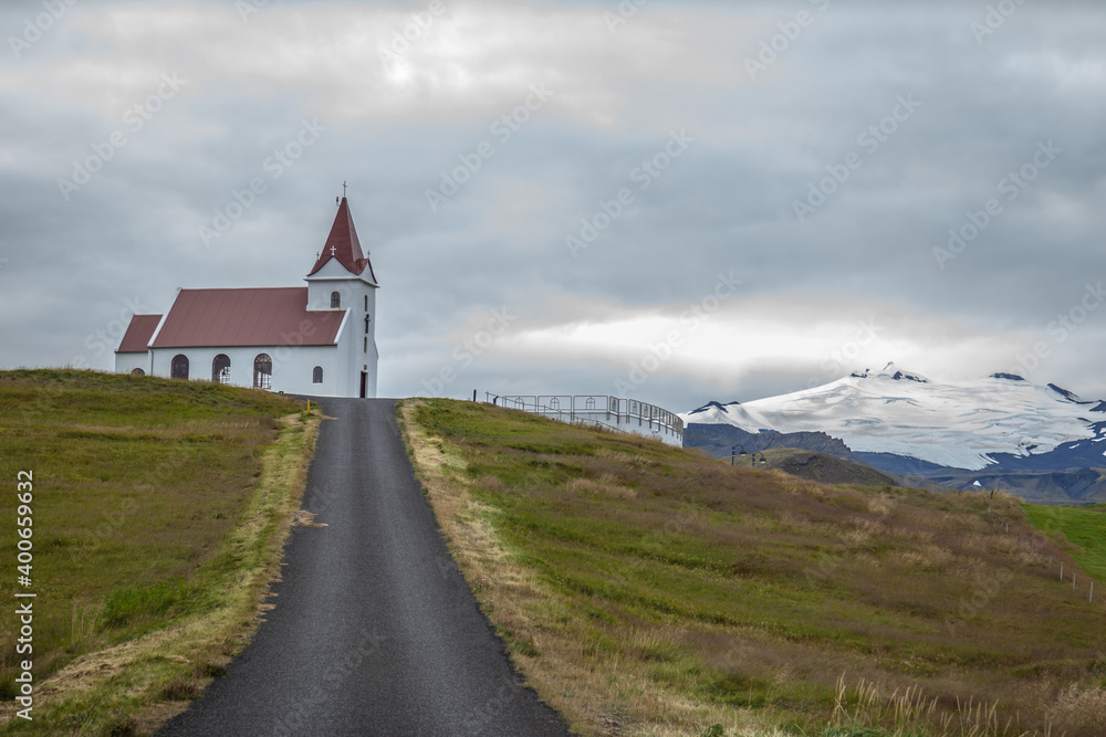 A road leading to Ingjaldsholl church with snow mountain in background at Hellisandur, on border of Snaefellsjokull National Park, Snaefellsnes Peninsula, Iceland.
