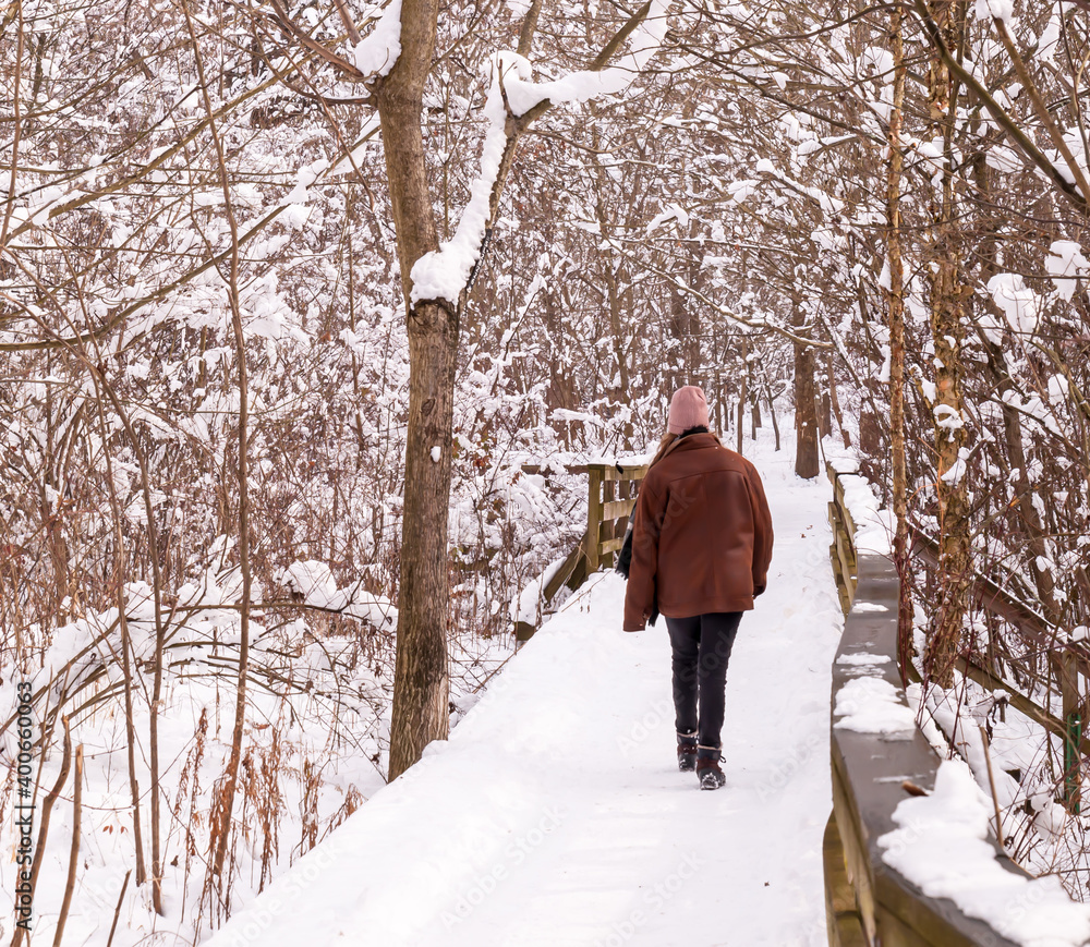 A man walking on a snow covered wooden bridge in winter time in Frick Park located in Pittsburgh, Pennsylvania, USA