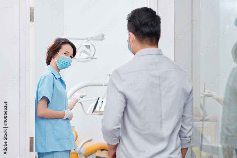 Fototapeta premium Smiling dental nurse inviting patient in office and asking him to sit in dental chair