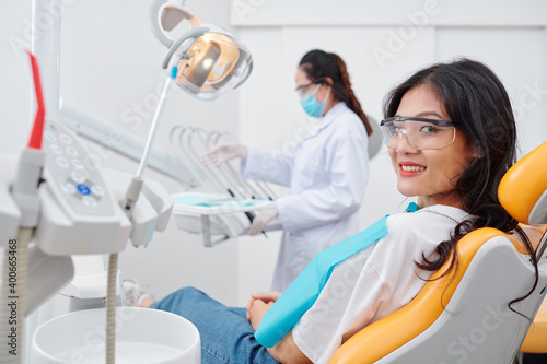 Pretty smiling young Vietnamese woman in goggles sitting in dental chair and looking at camera