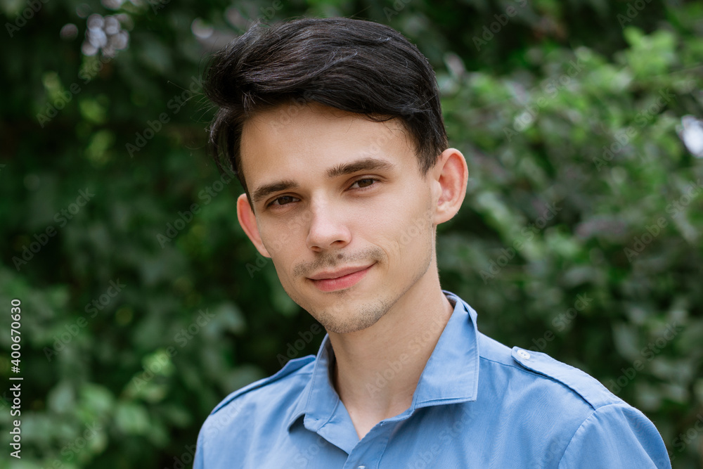 Portrait of a young man in a blue shirt on a green natural background Portrait of a young man in a blue shirt on a green natural background