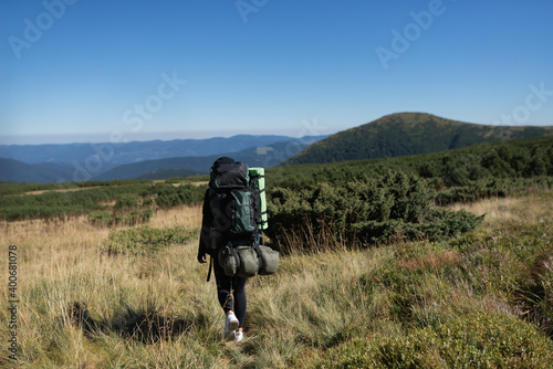 rear view of a young woman tourist with a large backpack is walking along the mountain plain. Hiking concept. banner.
