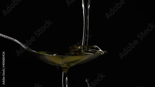 Close-up pouring olive oil liquid into spoon on black background in slow motion photo