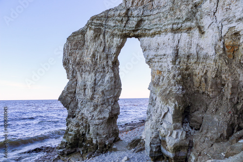 rocky stone arch from various natural rocks, on  river bank.  layered hollow stone arch on  pebble beach near  river.  unusual rock in  form of  arch or  gate of great height on the coast. © Оксана Скиданова